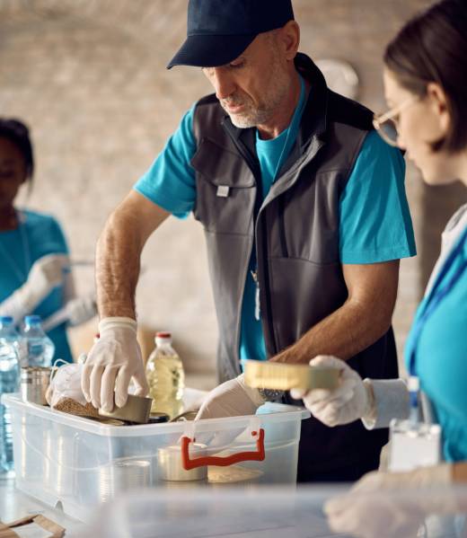 Mature man packing donated food into boxes while volunteering at humanitarian aid center.